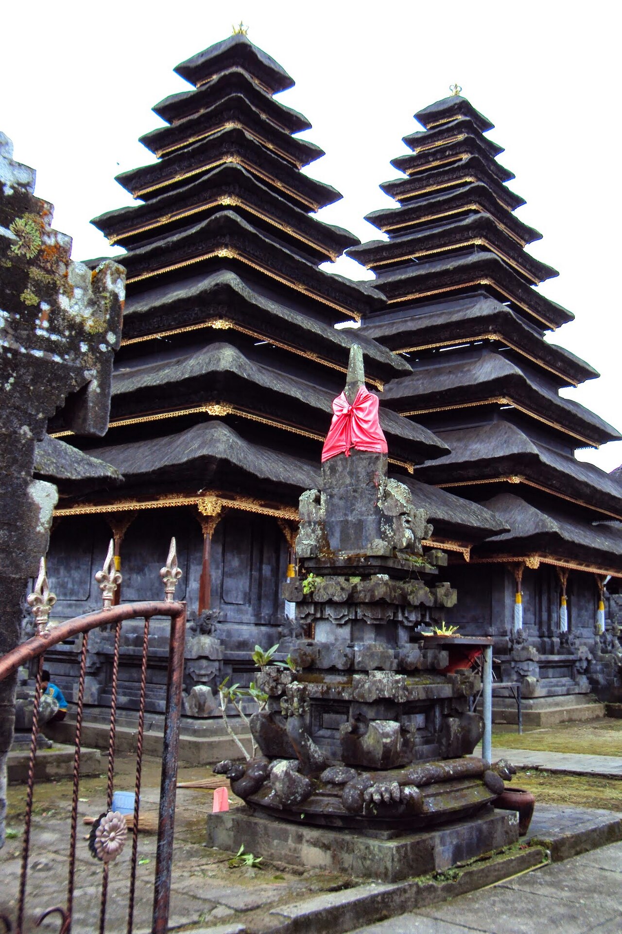 Meru towers of Pura Penataran Agung rising behind a stone shrine wrapped in red cloth at Besakih