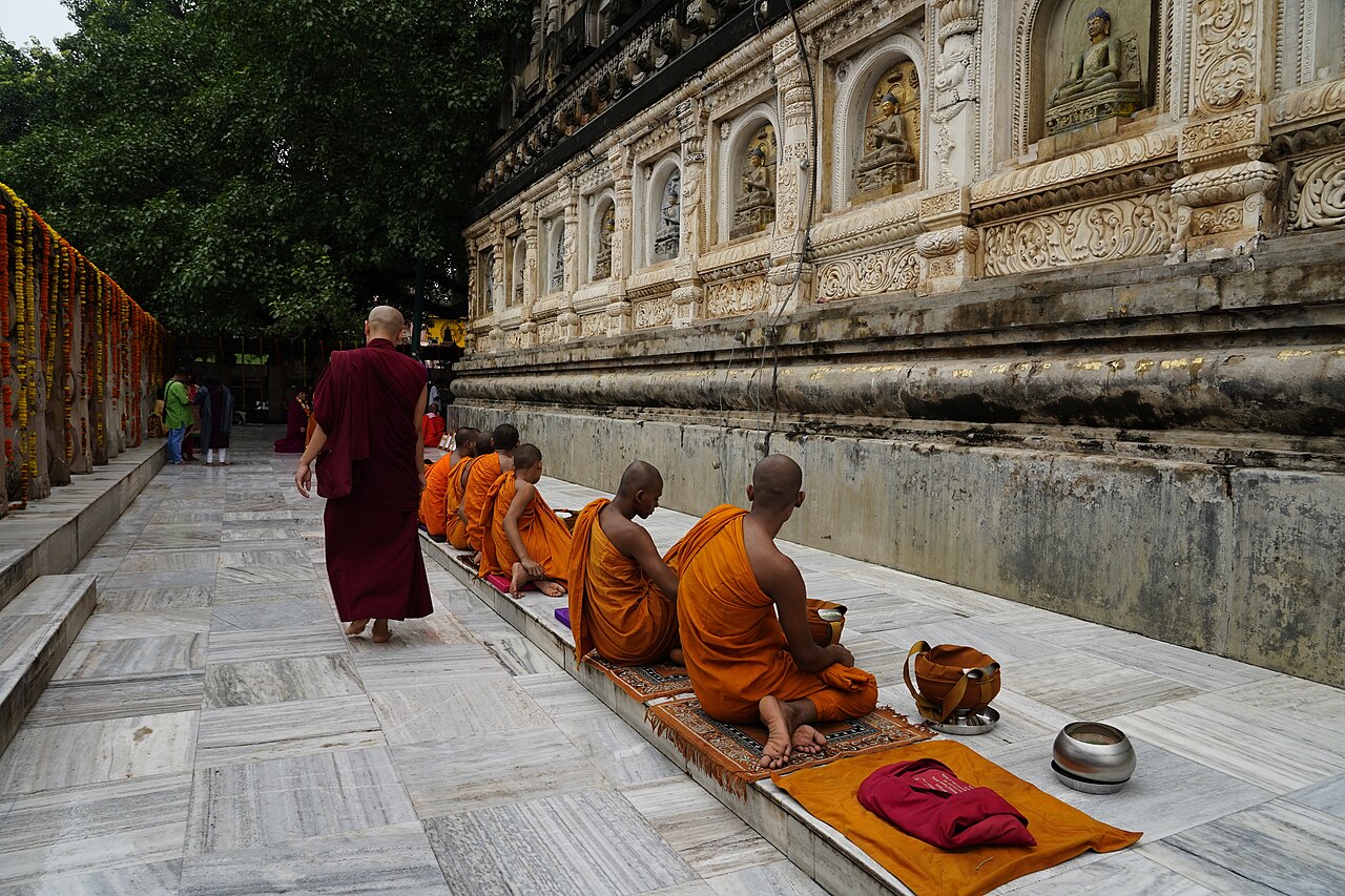 Bhikkhus seated in prayer beside the carved niches of the Mahabodhi Temple wall