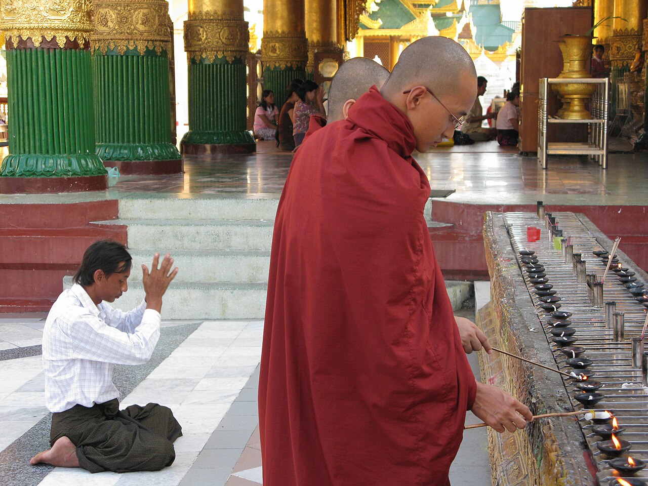 A devotee kneels in prayer on the marble platform before the gilded stupa of Shwedagon