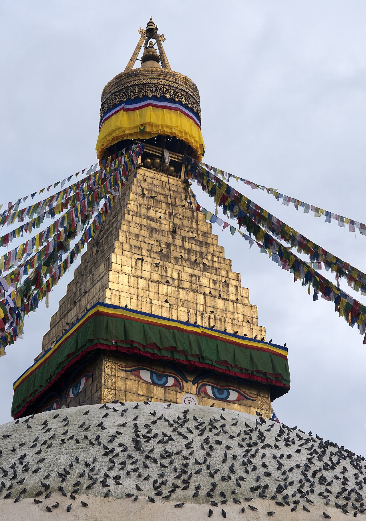 The Buddha eyes on the gilded harmika of Boudhanath, prayer flags streaming from the spire and pigeons resting on the whitewashed dome