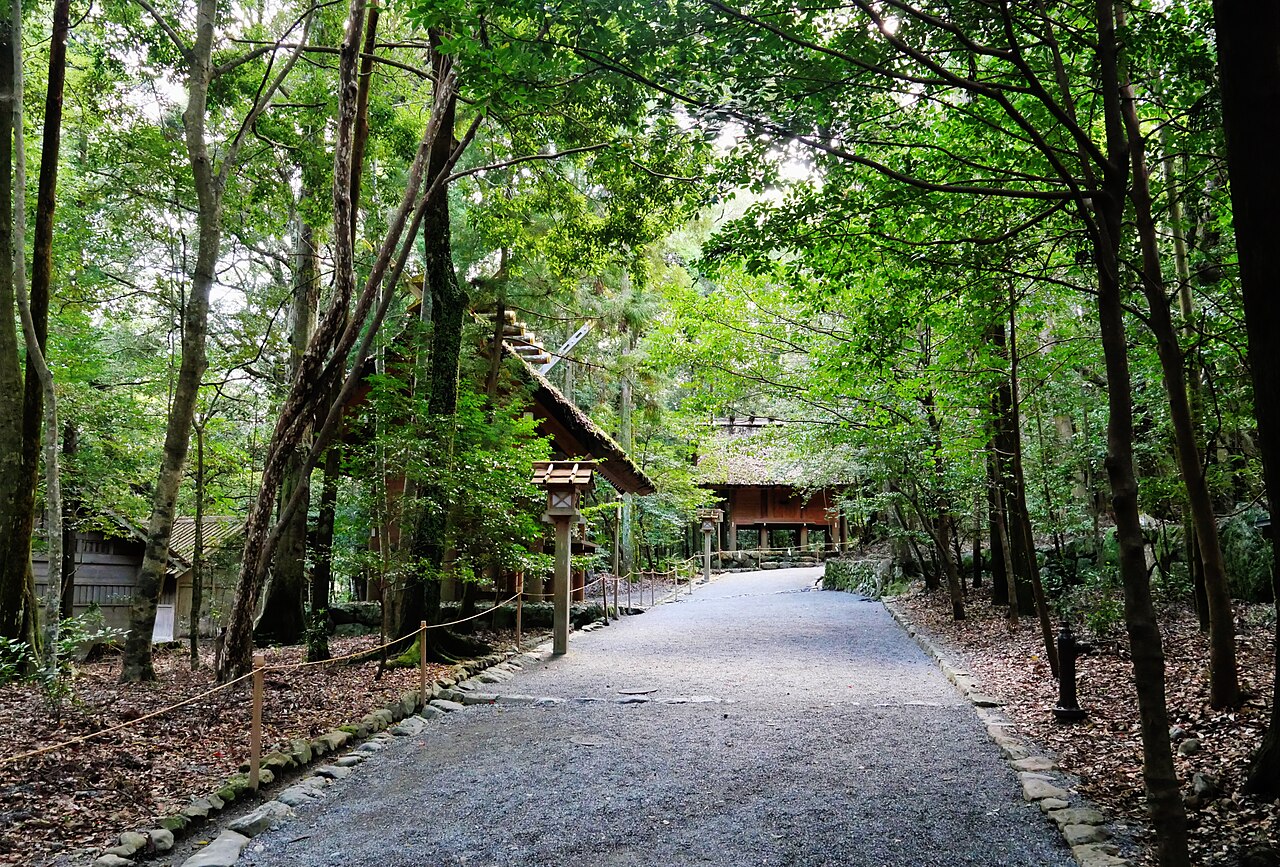 A gravel path through the shrine forest of Ise Jingu, lined with lanterns and thatched halls