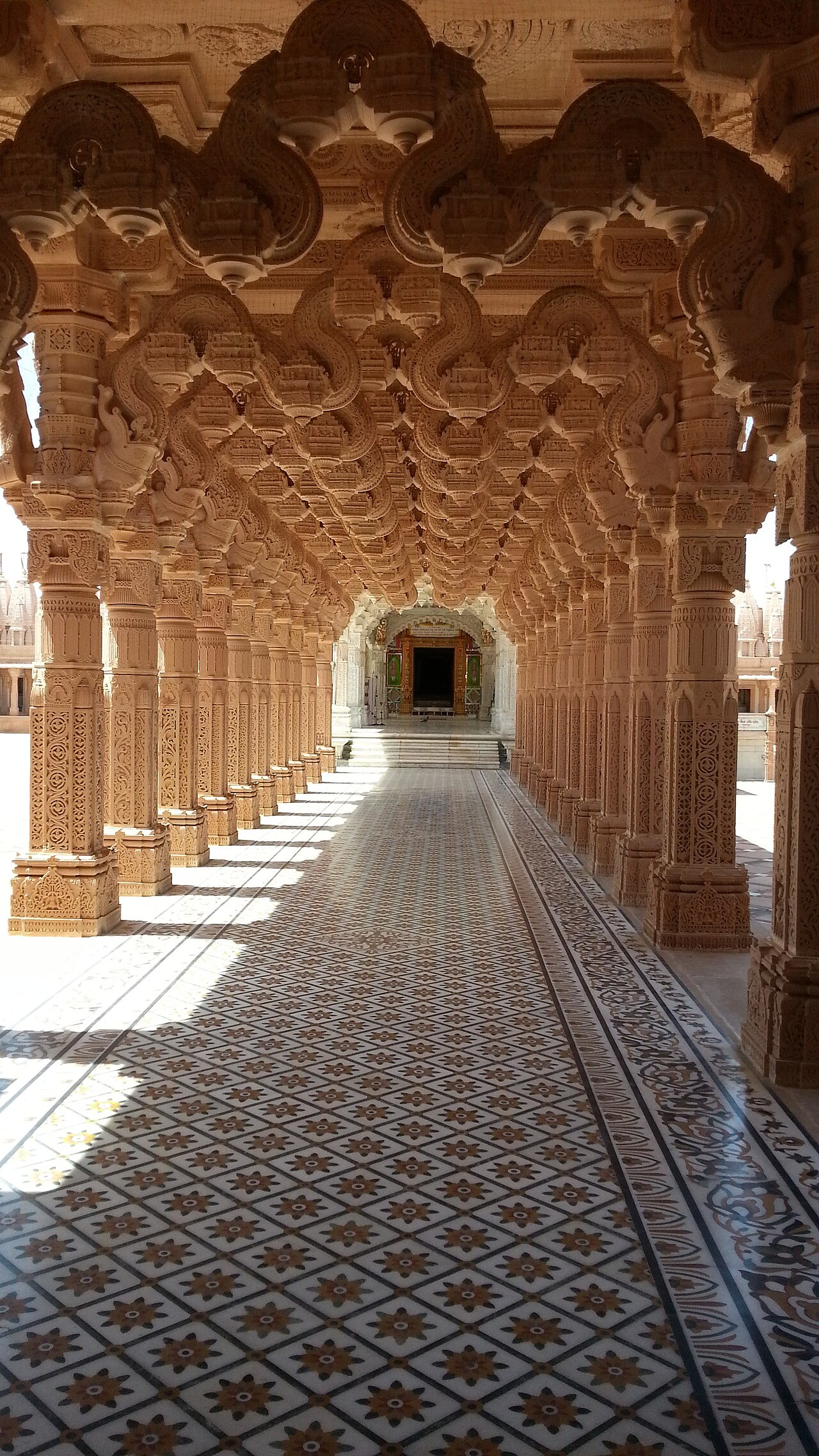 A pillared marble corridor at the 108 Parshwanath Bhaktivihar leads toward a shrine doorway