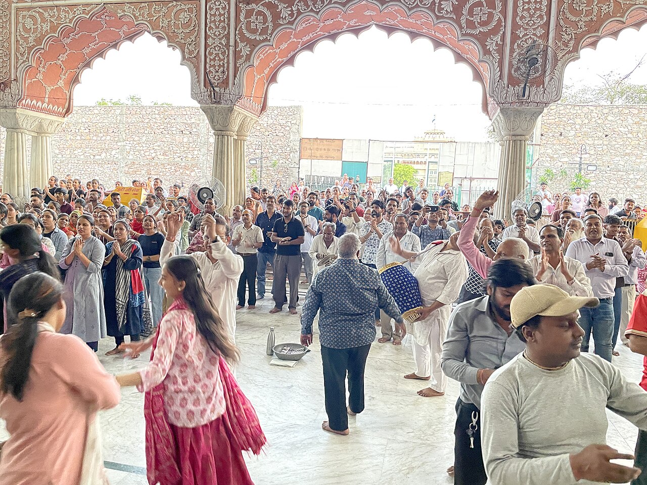 Devotees sing and clap under a carved pink arch in the Govind Dev Ji Temple courtyard during a kirtan gathering