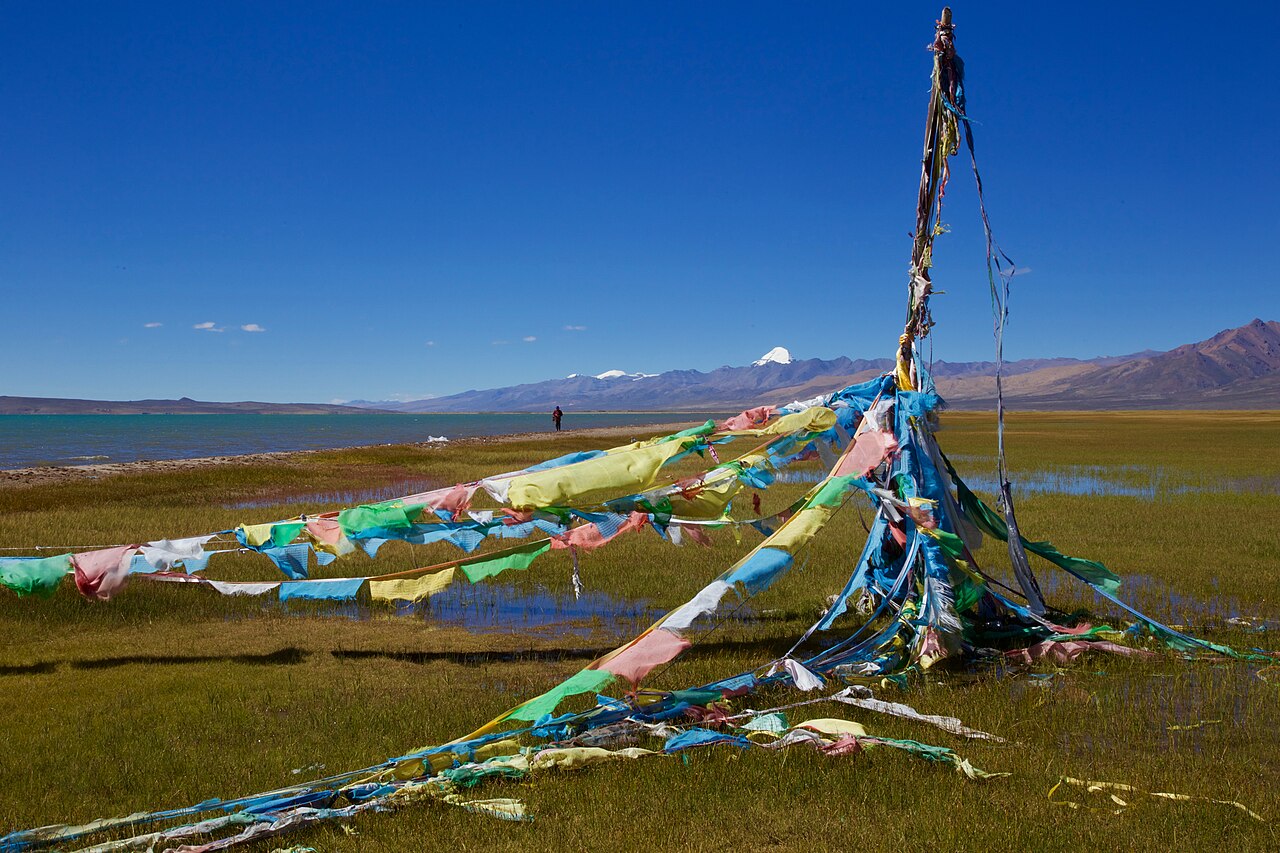 Prayer flags on the shore of Lake Mansarovar with the snow dome of Mount Kailash on the horizon