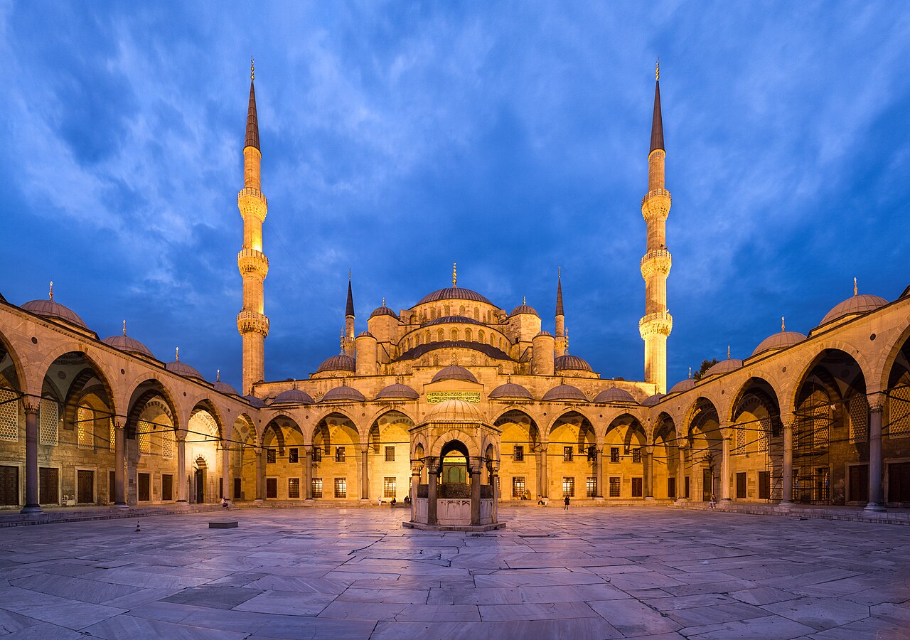The arcaded courtyard of the Sultan Ahmed Mosque at dusk, its domes and minarets lit against the sky