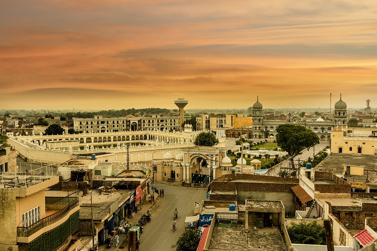 Gurdwara Janam Asthan's domes and marble colonnade rising above the rooftops and streets of Nankana Sahib at dusk