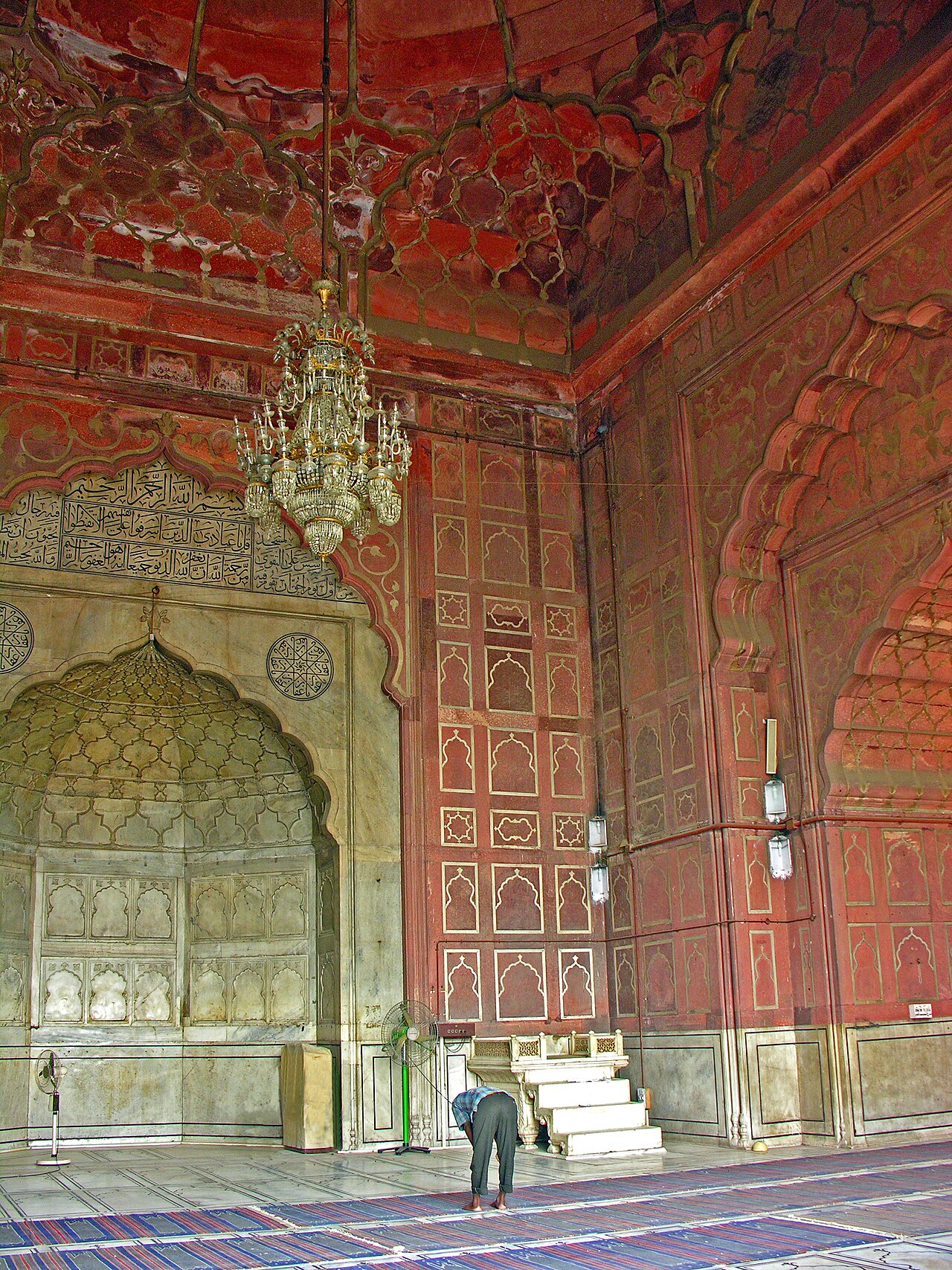 The marble mihrab and minbar of Jama Masjid's prayer hall, under painted vaults and a chandelier