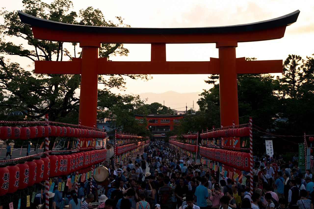 Crowds and rows of red lanterns beneath the first torii at dusk during the Motomiya-sai festival