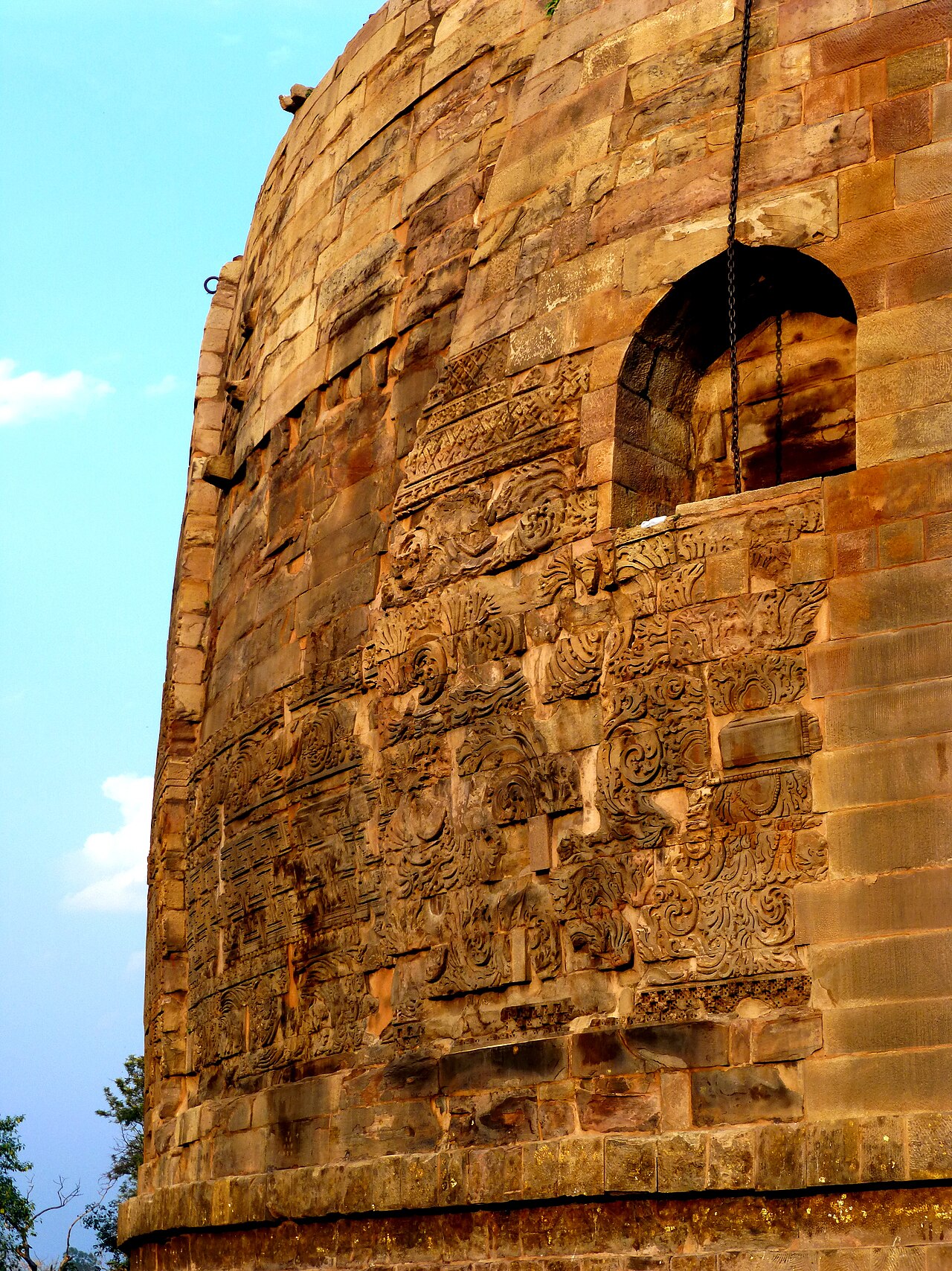 The transition from carved stone base to plain brick tower on the Dhamek Stupa, with an arched relic niche in the stonework