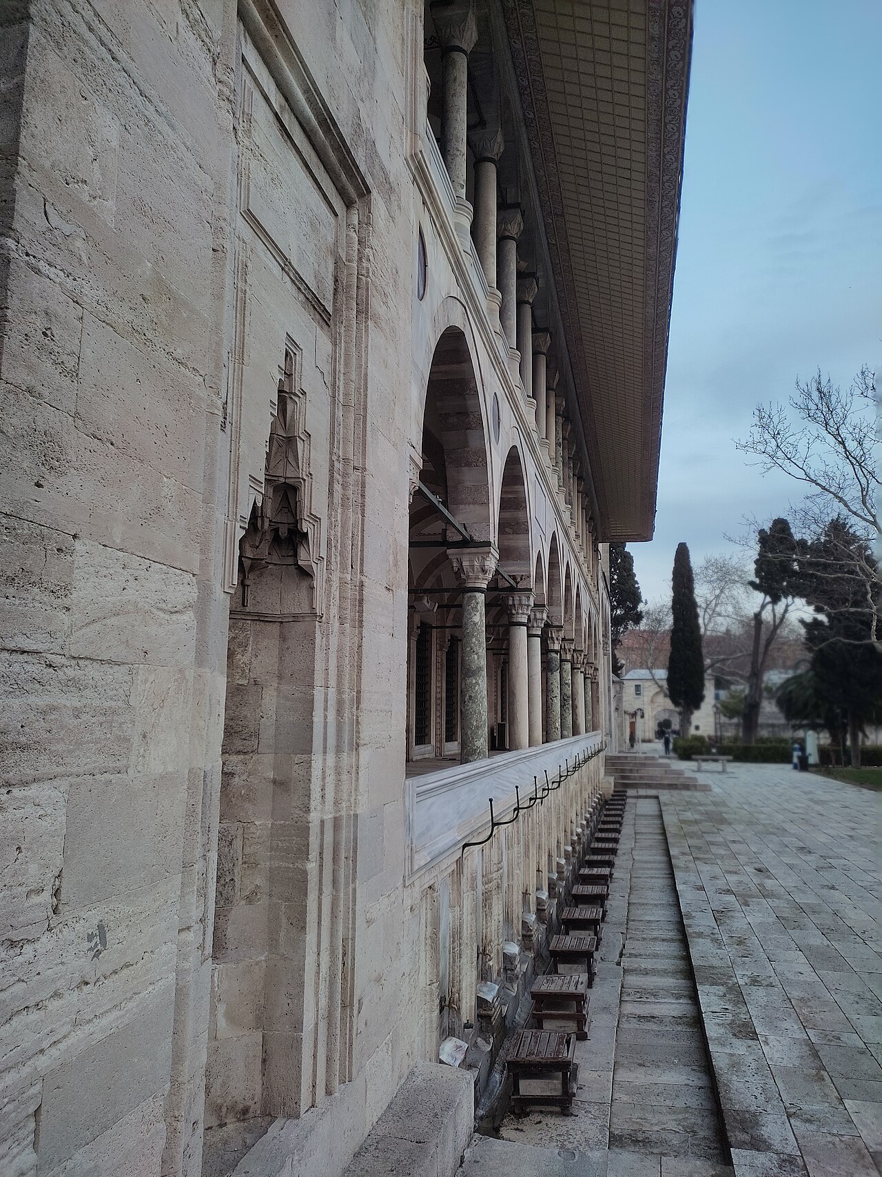 Brass ablution taps set into the marble outer wall of the Süleymaniye Mosque, with the arcaded gallery and courtyard behind
