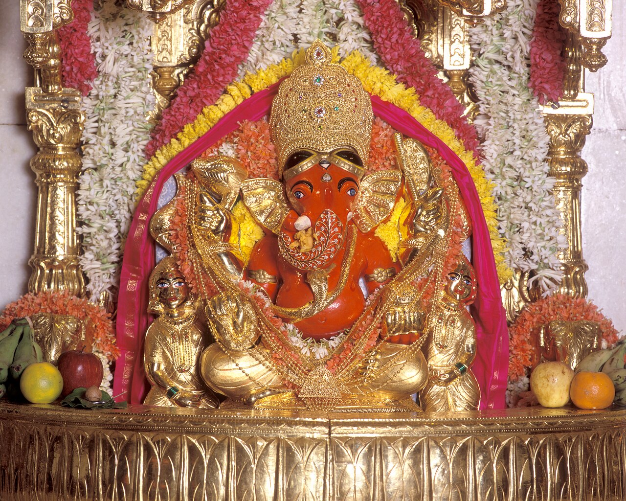 Shree Siddhivinayak in the sanctum, crowned and garlanded, with Riddhi and Siddhi in gold at His sides
