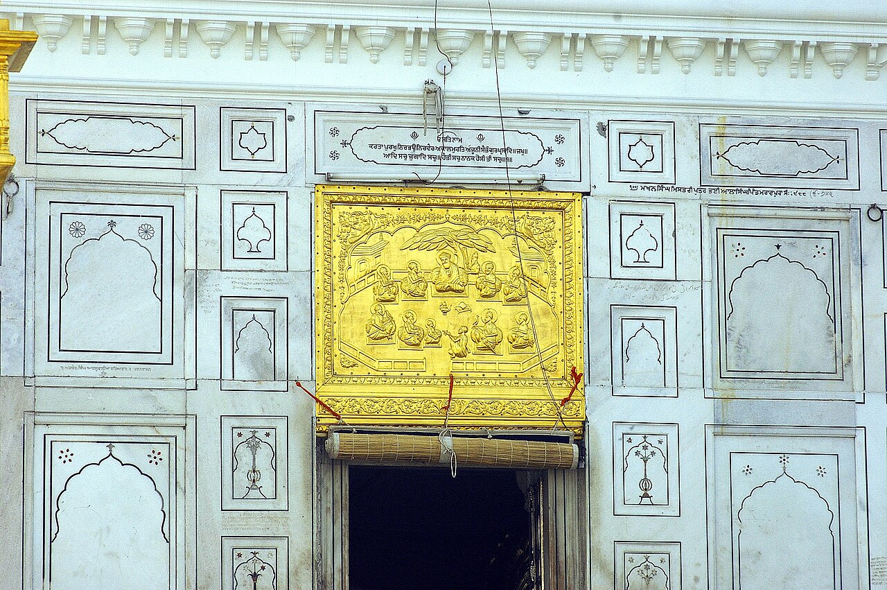 A gold relief panel over an entrance at Gurdwara Sri Tarn Taran Sahib, depicting the Sikh Gurus