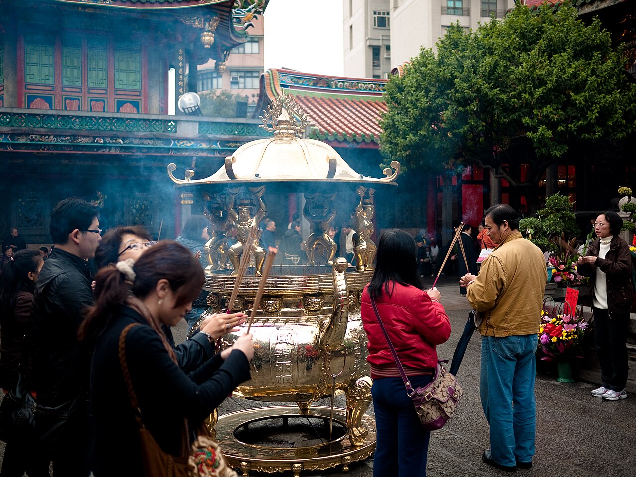Worshippers offering incense sticks around the great golden censer in the courtyard of Bangka Lungshan Temple