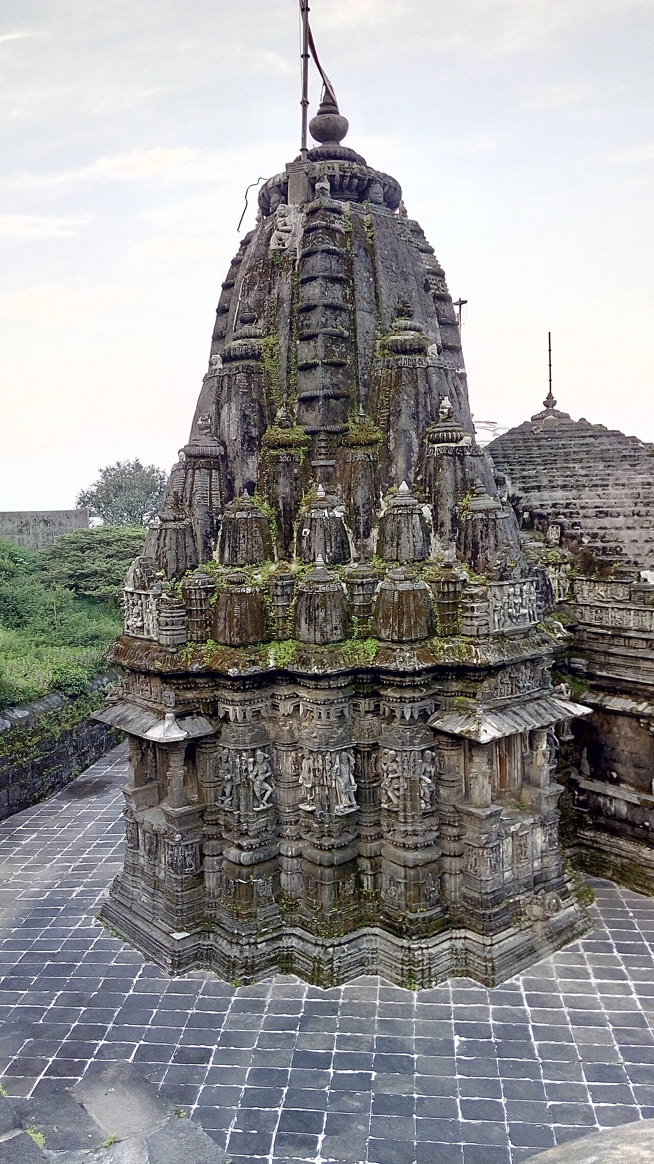 Close view of a carved dark granite shikhara at the Girnar Jain Temples, its tiers layered with small figures and moss