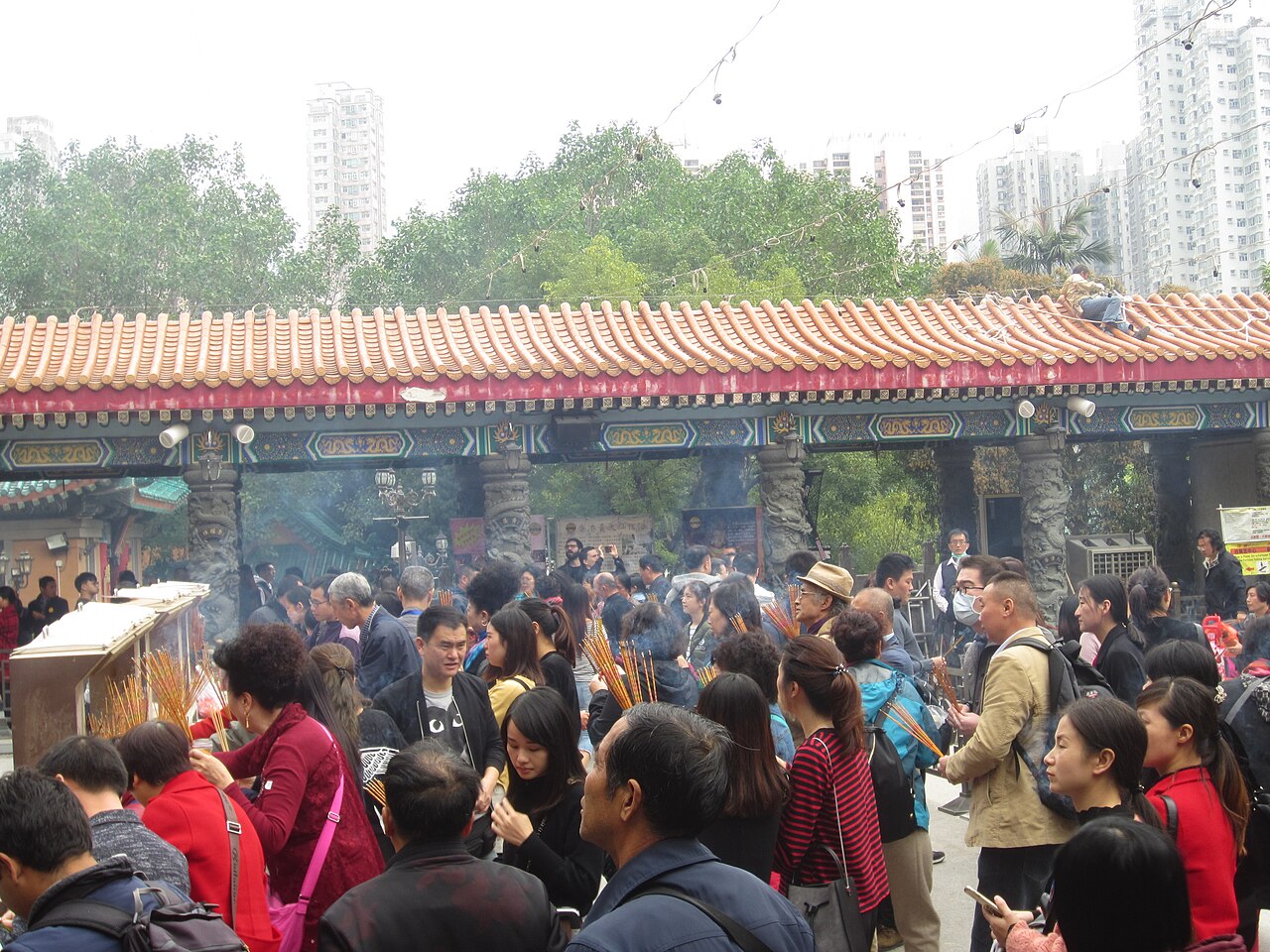 Devotees raising bundles of incense sticks amid smoke before the pillared gateway of Wong Tai Sin Temple
