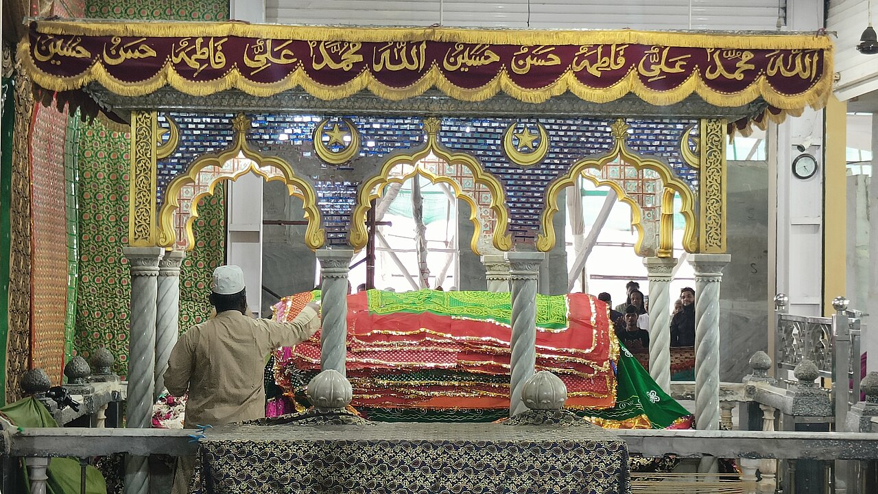 The mazar of Pir Haji Ali Shah Bukhari layered with red and green chadars beneath its canopied marble enclosure