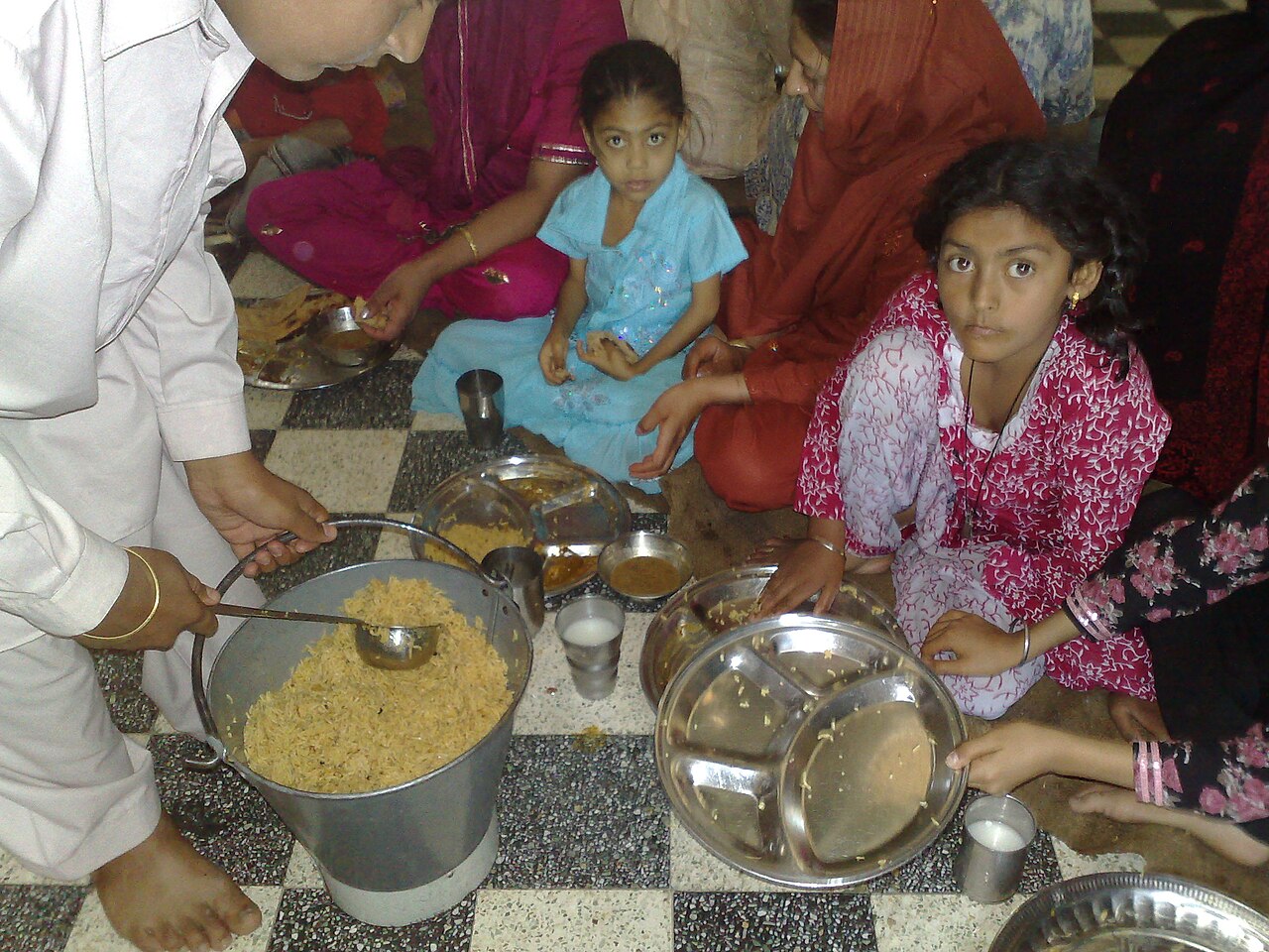 Langar being served from a large pot to families seated on the floor at Gurdwara Panja Sahib