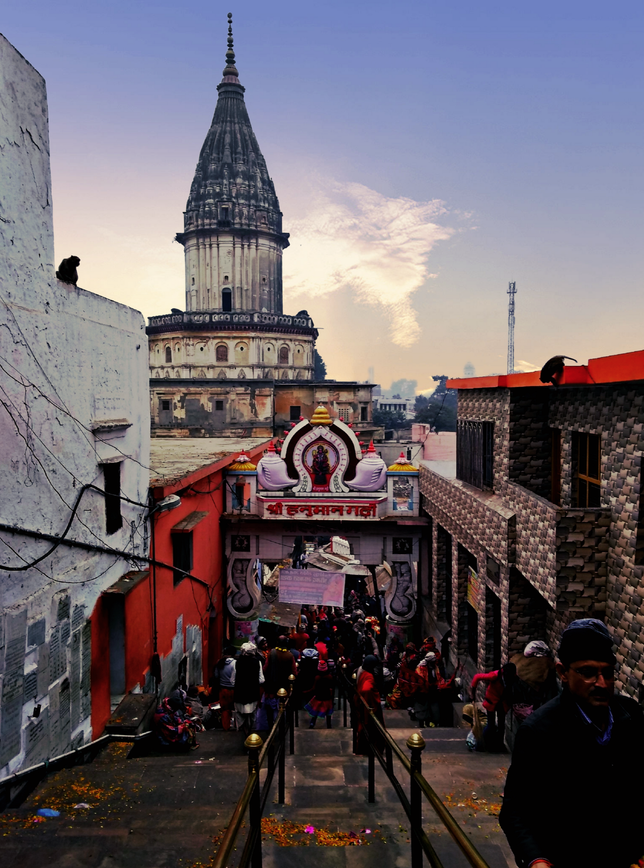 Looking down the 76 steps to the arched gateway of Hanuman Garhi at dusk, monkeys on the rooftops and the shikhara behind
