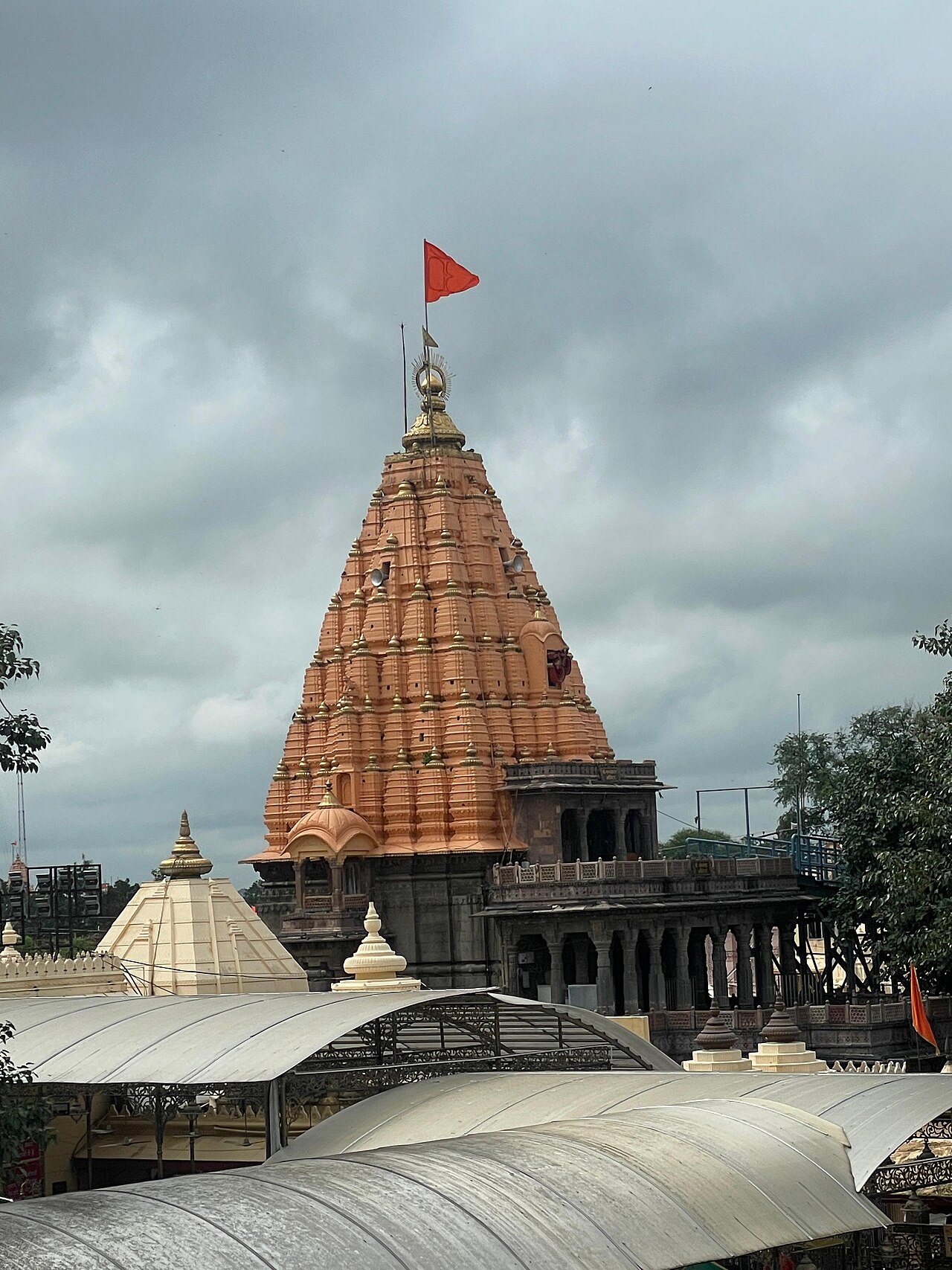 The shikhara of Shri Mahakaleshwar Temple with its saffron flag against a monsoon sky