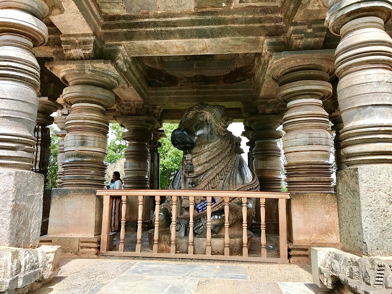 A colossal seated Nandi in its pillared pavilion at the Hoysaleswara Temple, facing the sanctum of Lord Shiva