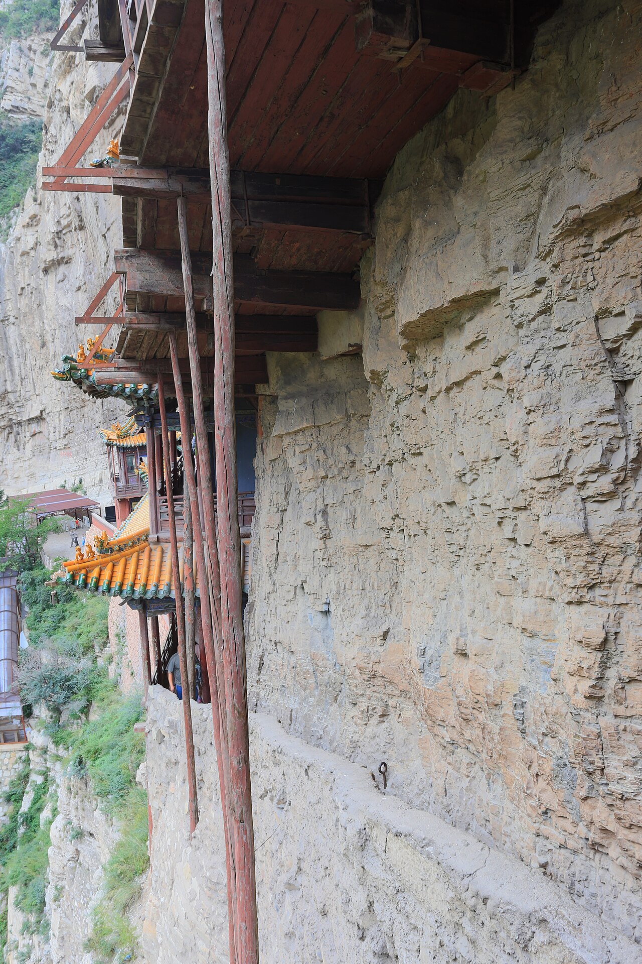 The walkway beams and slender wooden poles of the Hanging Temple seen edge-on along the rock face, with the gorge dropping away below