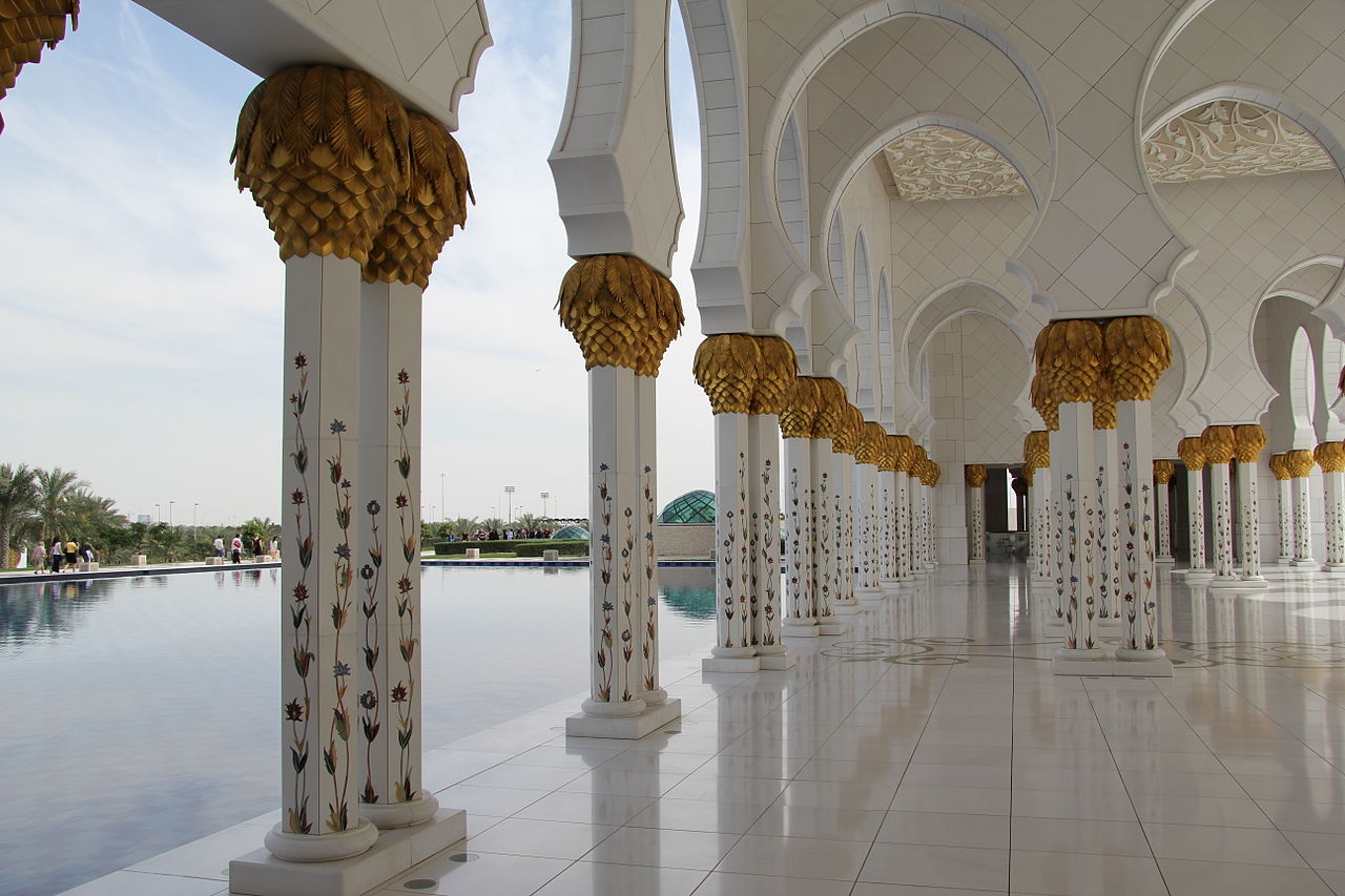 Columns crowned with golden palm fronds beside the reflective pool of Sheikh Zayed Grand Mosque